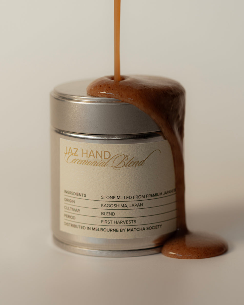 Matcha powder being poured into a container labeled 'Jaz Hand Ceremonial Blend' on a neutral background.